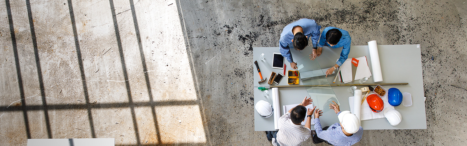 A team gathered around a table, revieing plans and blue prints, in a construction setting - aerial view.