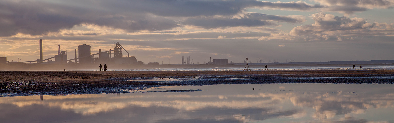 An image of a steel works in the background, with a river in the foreground and sky reflected in it.