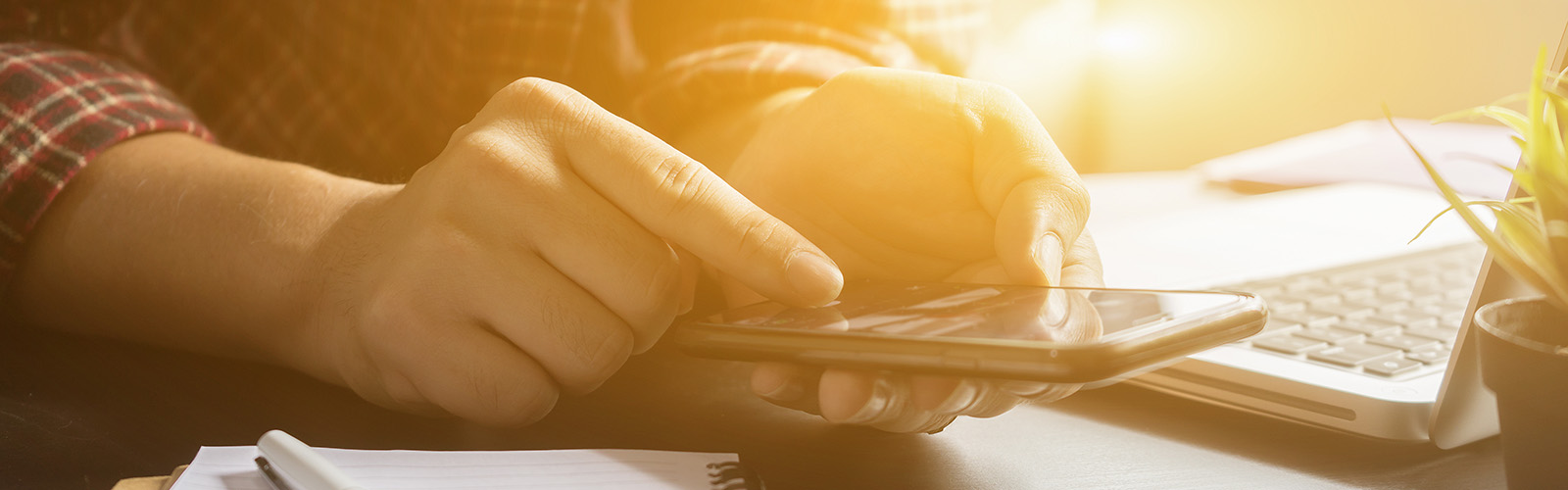 A person typing on their phone, zoomed in view, laptop in the background, in soft daylight